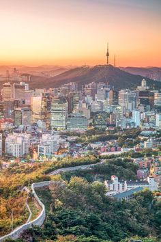 the city skyline is shown at sunset with mountains in the background and trees on both sides