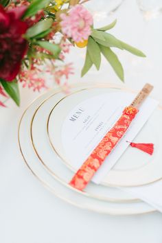 the place setting is set with white plates and gold rimmed cutlery, red flowers in vases