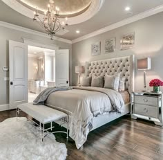 a bedroom with a large bed and chandelier on the ceiling, along with a white rug