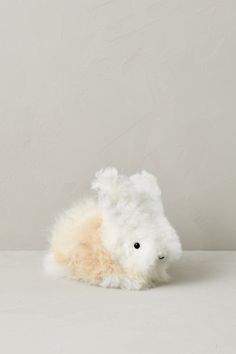 a white stuffed animal laying on top of a white table next to a gray wall