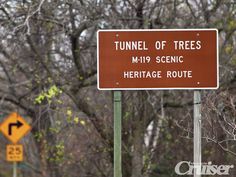 a brown sign sitting on the side of a road next to a tree filled forest