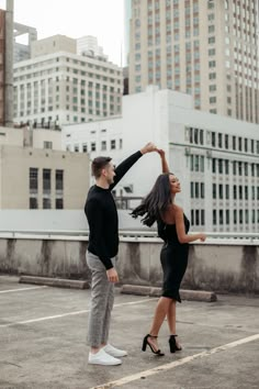 an engaged couple dancing in the middle of a parking lot with tall buildings behind them