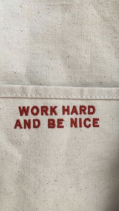 the back side of a white jacket with red lettering that says work hard and be nice