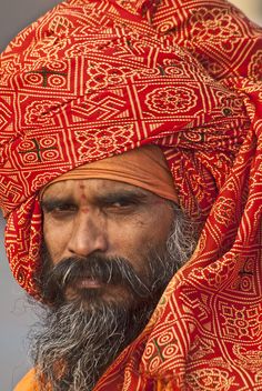 a man with a beard wearing a red turban and orange shawl on top of his head