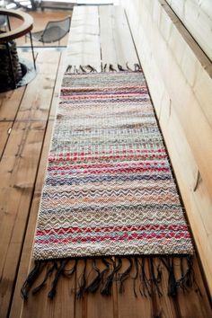 a multicolored rug is laying on the floor next to a wooden table and chair