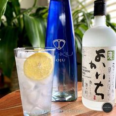 a bottle of alcohol next to a glass filled with ice and lemon slices on a wooden table