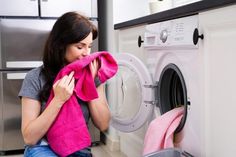 a woman sitting on the floor in front of a washing machine holding a pink towel