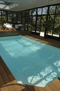 an empty swimming pool in front of a large glass walled windowed room with wood floors