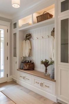 a white entryway with wooden flooring and built - in bench, coat rack, and purses