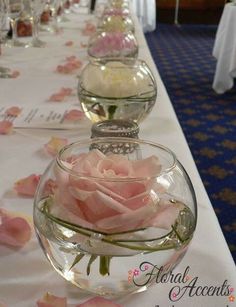 a long table with flowers in vases on the top and white clothed tables behind it