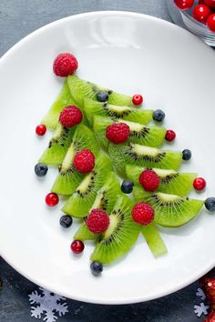 a white plate topped with kiwis and berries on top of snowflakes