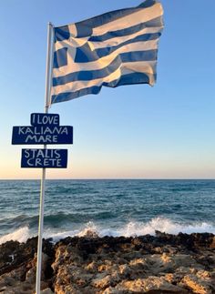 a greek flag flying over the ocean next to a sign that says i love kalaliana mare