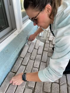 a woman is painting the side of a brick building with blue paint and white trim