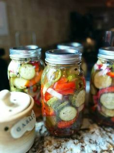 four jars filled with pickles and cucumbers