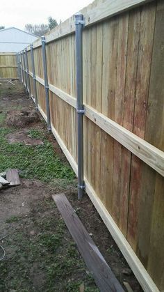 a wooden fence with metal posts on the side and grass in the yard behind it