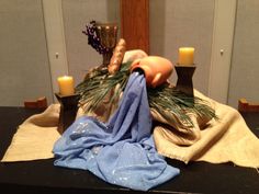 a table topped with candles and a vase filled with pine branches on top of a cloth