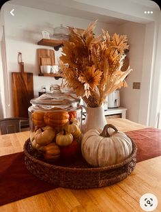 a table topped with a glass jar filled with pumpkins and gourds