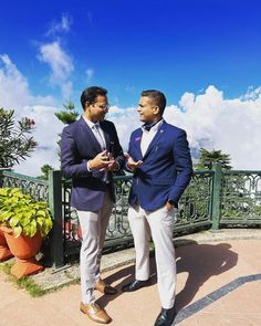 two men standing next to each other in front of a green fence and blue sky