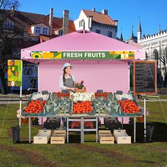 a woman selling fresh fruits at an outdoor stand in front of some buildings and trees