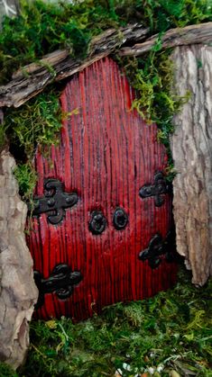 a red door is in the middle of some rocks and grass with moss growing on it