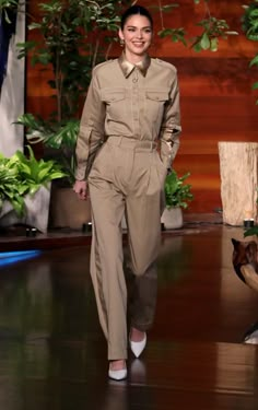 a woman is walking down the runway wearing a tan jumpsuit and white shoes with her hands in her pockets