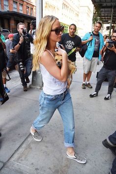 a woman walking down the street while holding a small dog in her lap and wearing sunglasses