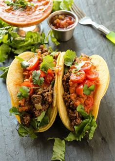 two tacos with meat, tomatoes and cilantro on a table next to salsa