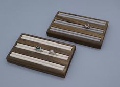 two wooden jewelry boxes with white candles and rings in them on a gray surface,