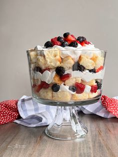 a trifle with berries, cream and blueberries in a glass dish on a wooden table