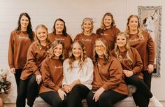 a group of women sitting next to each other wearing brown sweatshirts and black pants