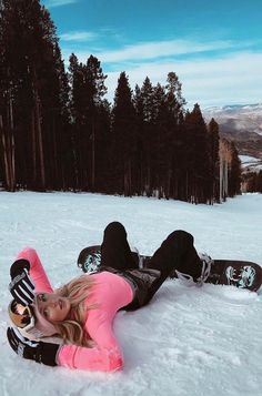 a woman laying in the snow on her stomach with a snowboard next to her