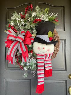 a christmas wreath with a snowman head hanging from the front door, decorated with red and white striped ribbon