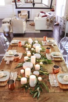 a wooden table topped with lots of white candles and greenery on top of it