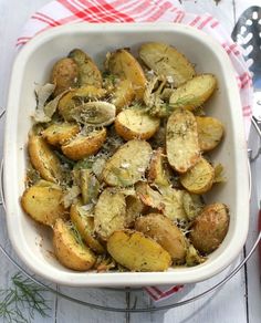 a white dish filled with potatoes covered in parmesan cheese and sprinkled with herbs