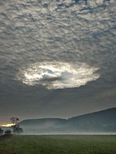 the sun is shining through the clouds in the sky over an open field with trees