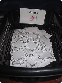 a pile of stamps sitting in a black basket on top of a wooden table next to a sign that says stamps