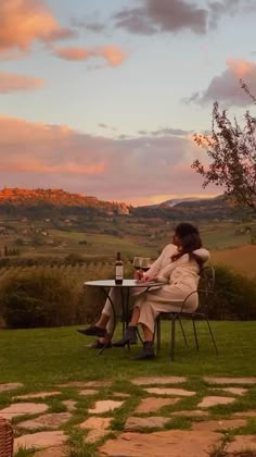 a woman sitting at a table with a bottle of wine in front of her on the grass