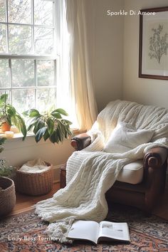 an open book is sitting on a chair in front of a window with a blanket draped over it