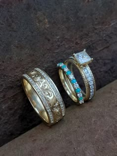 two gold rings with diamonds and turquoise stones on them sitting next to each other in front of a stone wall