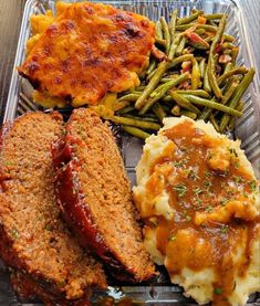 a plastic container filled with meat, mashed potatoes and gravy next to green beans