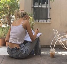 a woman sitting on the ground writing with a pen and paper in front of her