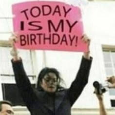 a woman holding up a pink sign that says today is my birthday with other people behind her