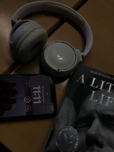 an mp3 player, book and headphones are on a table next to a cell phone