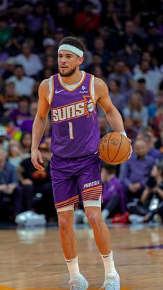 a man holding a basketball while standing on top of a wooden floor in front of a crowd