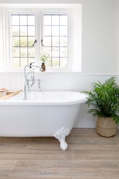 a white bath tub sitting next to a window with potted plants on the side