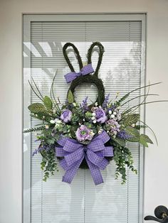 a wreath with purple flowers and greenery hanging on the front door