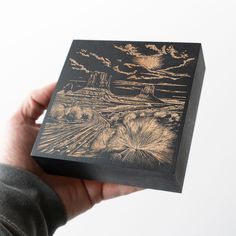 a person holding up a wooden box with an image of a desert scene on it