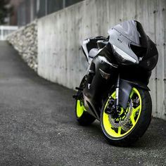 a black and yellow motorcycle parked in front of a wall on the side of a road