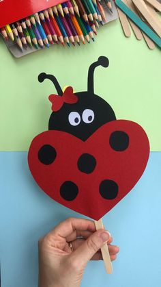 a ladybug shaped paper craft being held by a person with colored pencils in the background