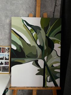 an easel with a painting on top of it next to a white table and gray wall